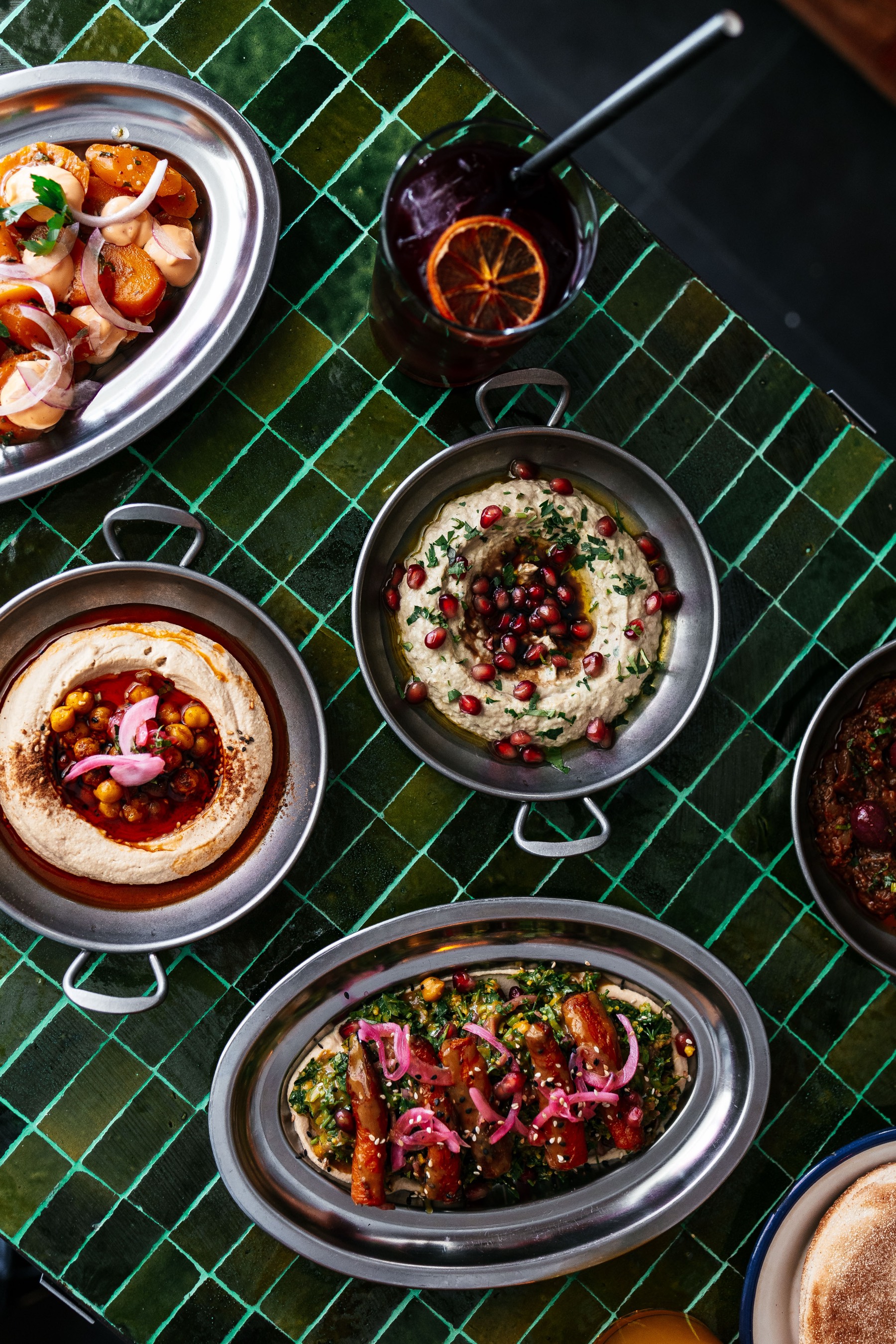 Mesa de azulejos verdes con hummus, couscous y zanahorias a la chermoula, vista desde arriba